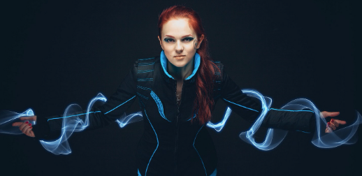 Futuristic red-haired woman in a black and blue high-tech suit with glowing electric stream trails extending from her arms, symbolizing empowerment and innovation in fashion.